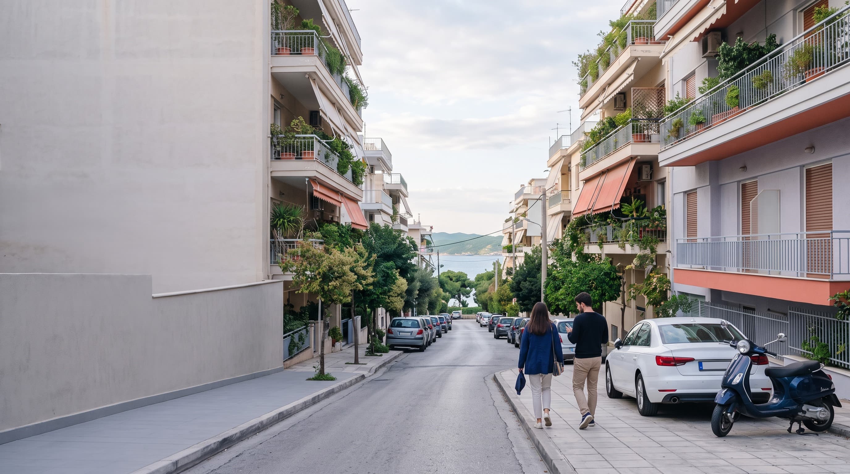 A sunlit residential street in Athens with a parked car and a neoclassical entrance